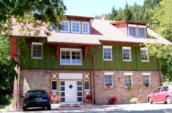 Fassade des Landgasthof-Pension Limbacher M&uuml;hle mit gr&uuml;nem Fachwerk, roten Fensterl&auml;den, mehreren Fenstern und geparkten Autos davor.