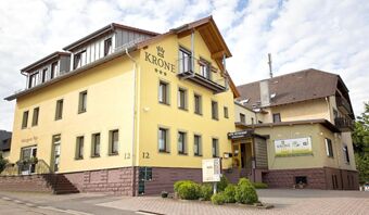 Fasada rumene stavbe hotela Krone z več okni, majhnim balkonom in vhodom v hotelsko restavracijo.