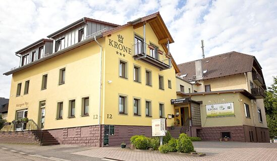 Fasada rumene stavbe hotela Krone z več okni, majhnim balkonom in vhodom v hotelsko restavracijo.
