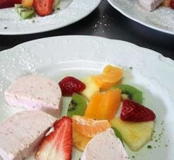 Sveža sladica z jagodami, kivijem, mandarinami in porcijo pene, postrežena na belem krožniku v hotelu Krone.