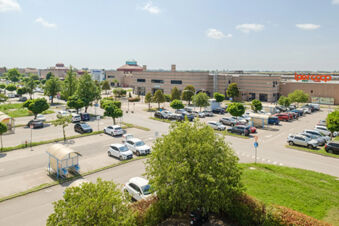 parking lot with cars and trees near a large shopping center building with an ipercoop sign viewed from B&B Hotel Ferrara