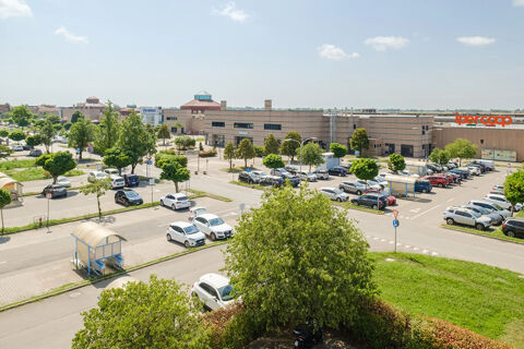 parking lot with cars and trees near a large shopping center building with an ipercoop sign viewed from B&B Hotel Ferrara
