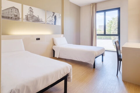 Hotel room at B&B Hotel Ferrara with two single beds, white bedding, framed black and white photos, and a window with curtains