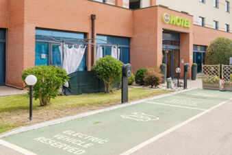Parking spaces marked electric vehicle reserved with charging stations in front of B&B Hotel Ferrara building and entrance