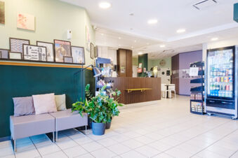 Waiting area with couches, cushions, potted plants, artwork, a reception desk, and a vending machine inside B&B Hotel Ferrara