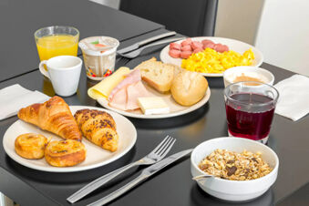 Breakfast spread with croissants, pastries, bread, ham, cheese, scrambled eggs, sausages, orange juice, coffee, yogurt, and cereal at B&B Hotel Ferrara