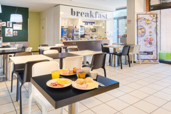 Modern breakfast area with tables, chairs, plates of food, and beverage station inside B&B Hotel Ferrara