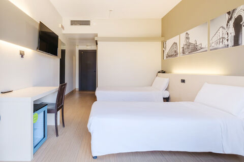 Hotel room at B&B Hotel Ferrara with two single beds, a desk, chair, wall-mounted TV, and black and white city photos on the wall