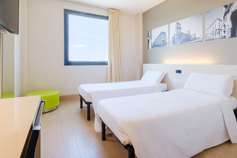 Two single beds with white linens in a bright room at B&B Hotel Ferrara featuring a window and three black and white framed photos