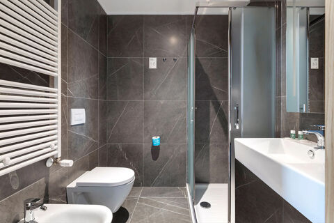 Modern bathroom with grey tiles, a wall-mounted toilet, bidet, shower area, and white sink at B&B Hotel Ferrara