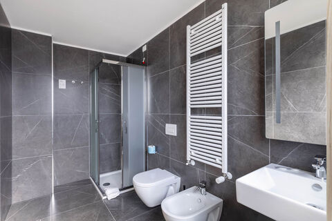 Modern bathroom with gray tiled walls, shower with frosted glass doors, toilet, bidet, and white sink at B&B Hotel Ferrara