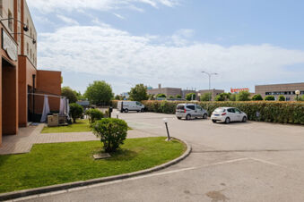 Parking area with three cars, green bushes, and part of a brick building near B&B Hotel Ferrara under a partly cloudy sky