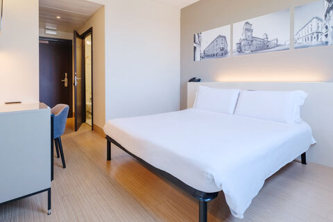 Simple hotel room at B&B Hotel Ferrara with a double bed, white linens, wooden flooring, and black-and-white wall photos