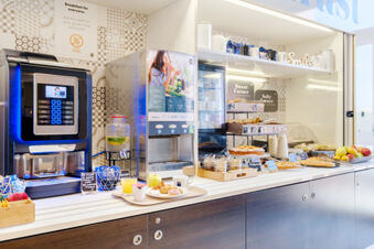 Breakfast buffet with coffee machine, juice dispenser, pastries, fruits, and cereals at B&B Hotel Ferrara