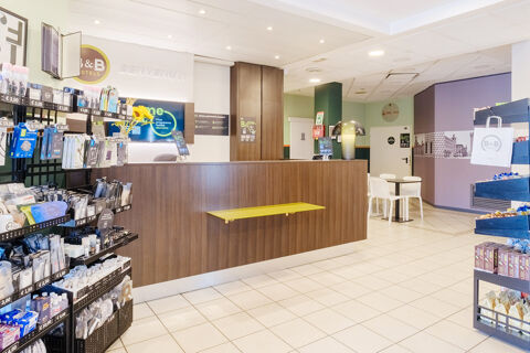 Reception desk with a yellow shelf, merchandise racks, and a seating area inside the B&B Hotel Ferrara lobby