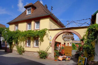 Yellow two-story building with tiled roof and green vines around windows and G&auml;stehaus Blank sign on archway entrance