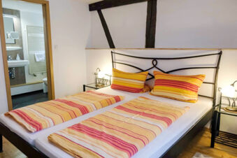 Bed with yellow and red striped bedding and pillows in G&auml;stehaus Blank with bedside tables and lamps visible