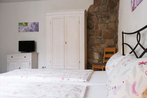 Bed with floral linens and black metal headboard beside wooden wardrobe and TV in a G&auml;stehaus Blank room