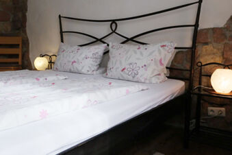 Double bed with floral bedding, black metal frame, two bedside tables with round lamps in G&auml;stehaus Blank bedroom