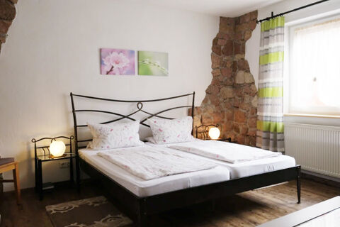A double bed with floral bedding and pillows in a room at G&auml;stehaus Blank with two nightstands and stone wall accents