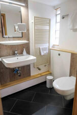 Bathroom at G&auml;stehaus Blank with white wall-mounted sink, mirror, towel radiator, and a white toilet next to a small window