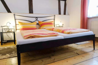 Double bed with striped yellow and orange bedding and pillows in a G&auml;stehaus Blank room with wood floors and nightstands with lamps