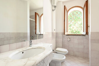 Bathroom interior at B&B HOTEL Ischia San Nicola with marble sink countertop, white toilet, bidet, and an open window with metal grate