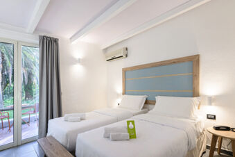 Two single beds with white linens and towels in a bright room at B&B HOTEL Ischia San Nicola with sliding doors to a terrace