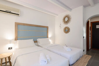 A bright hotel room at B&B HOTEL Ischia San Nicola with two single beds, white linens, wooden decor, and wall mirrors