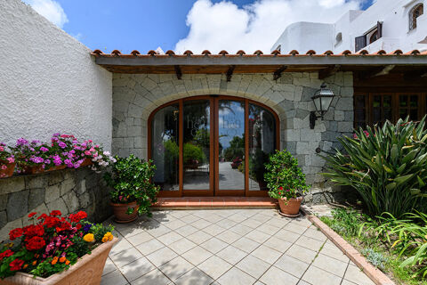 Entrance of B&B HOTEL Ischia San Nicola with stone wall facade, arched wooden glass doors, potted plants, and greenery under blue sky