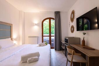 Bedroom with a large bed, white linens, towels, wooden desk and chair, wall-mounted TV, and balcony door at B&B HOTEL Ischia San Nicola