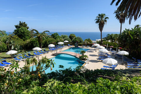 Swimming pool with blue sun loungers, white umbrellas, palm trees, and ocean view at B&B HOTEL Ischia San Nicola
