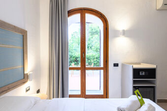 Interior of a clean, modern hotel room with white bedding, wooden arched door, and a safe cabinet at B&B HOTEL Ischia San Nicola