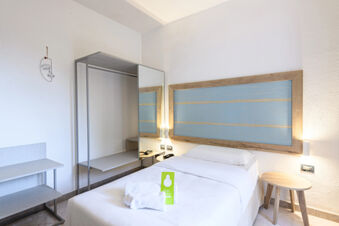 Single bed with white linens and towels placed on it, wooden bedside table and open wardrobe in B&B HOTEL Ischia San Nicola room