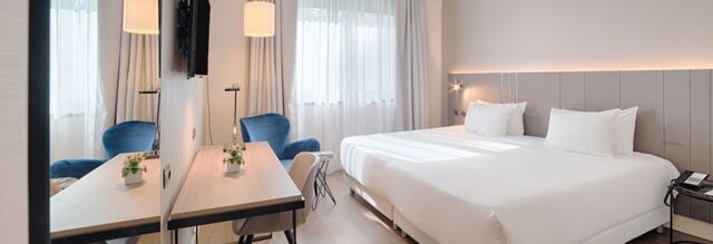 Bright hotel room at Hotel NH Roma Villa Carpegna with a double bed, white linens, desk, blue armchair, and window curtains