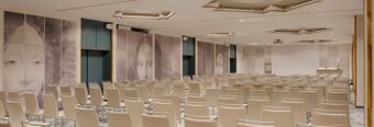 Conference room with rows of beige chairs, large wall murals of faces, and a white projector screen at Hotel NH Roma Villa Carpegna