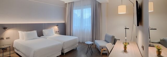 Hotel NH Roma Villa Carpegna room with two single beds, bedside tables, a sofa, desk, chair, and window with curtains