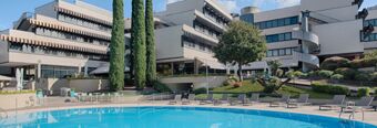 Outdoor pool area with lounge chairs, tables, trees, and modern white buildings at Hotel NH Roma Villa Carpegna
