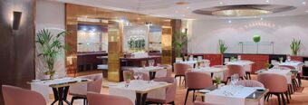 Dine area with pink chairs, tables set with white tablecloths, glassware, and plants at Hotel NH Roma Villa Carpegna
