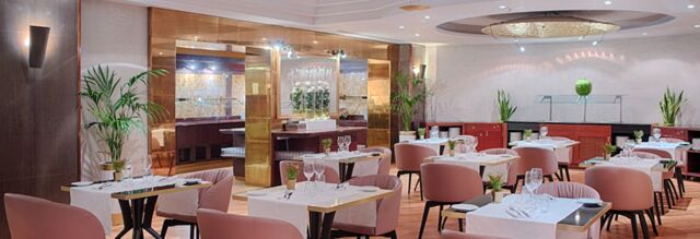 Dine area with pink chairs, tables set with white tablecloths, glassware, and plants at Hotel NH Roma Villa Carpegna
