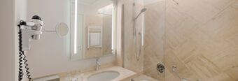 Bathroom with a sink, mirror, hairdryer, glass shower cabin, and towel rack in Hotel NH Roma Villa Carpegna