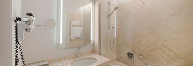 Bathroom with a sink, mirror, hairdryer, glass shower cabin, and towel rack in Hotel NH Roma Villa Carpegna