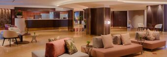 Spacious hotel lobby with modern seating arrangements, plants, and reception desk at Hotel NH Roma Villa Carpegna