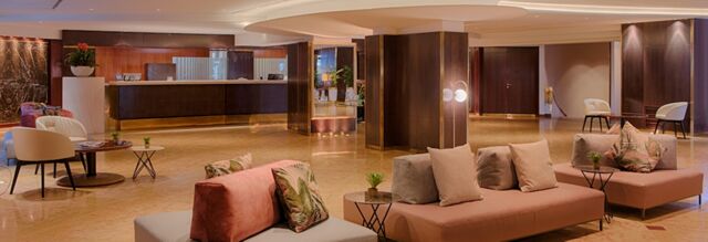 Spacious hotel lobby with modern seating arrangements, plants, and reception desk at Hotel NH Roma Villa Carpegna