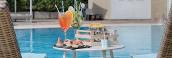 Two colorful cocktails with straws and snacks on a white table by the poolside at Hotel NH Roma Villa Carpegna