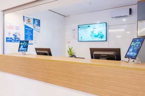 Reception desk with two computer monitors and digital tablets at B&B Hotel Ravenna with promotional posters on the wall