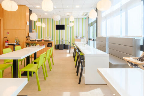 Bright dining area at B&B Hotel Ravenna with white tables, green and black chairs, booth seating, and hanging lights