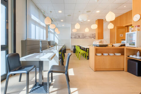 Dining area with white tables, black and green chairs, pendant lights, and a breakfast counter at B&B Hotel Ravenna