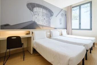 Three single beds with white linens and a study desk with chair in a room at B&B Hotel Ravenna