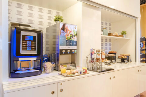 Coffee machines with a breakfast display of juice, pastries, cereals, and fruits at B&B Hotel Ravenna buffet station
